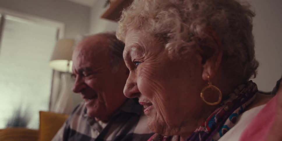 2 elderly people sitting on the sofa talking to someone and are happy