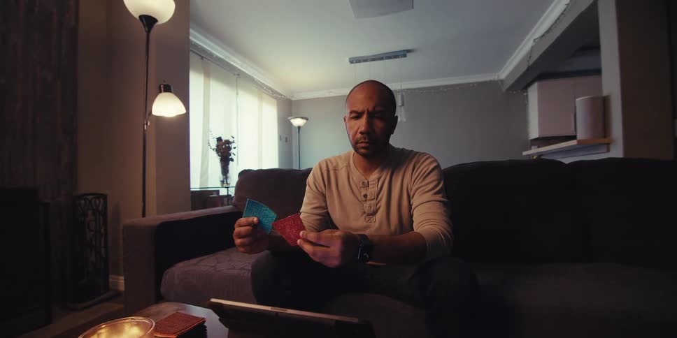 A man is sitting on the couch looking down at his tablet