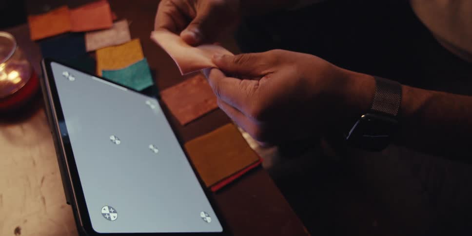 A man is sitting on a couch in front of a tablet and looking at swatches