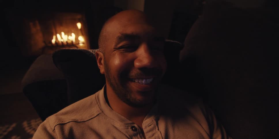 Man lying on the sofa looking at something on his smartphone and smiling