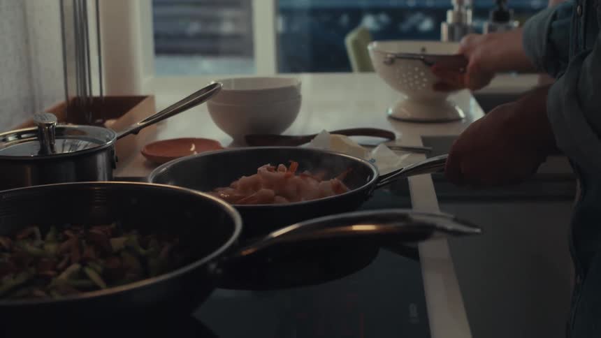 Man cooking in the kitchen with his wife adds shrimp to a skillet
