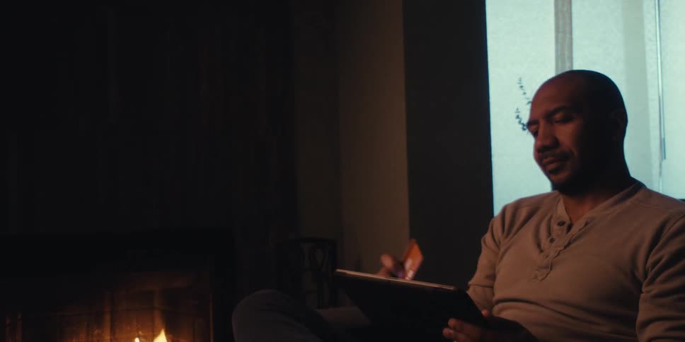 A man walks around and uses his tablet by the fireplace