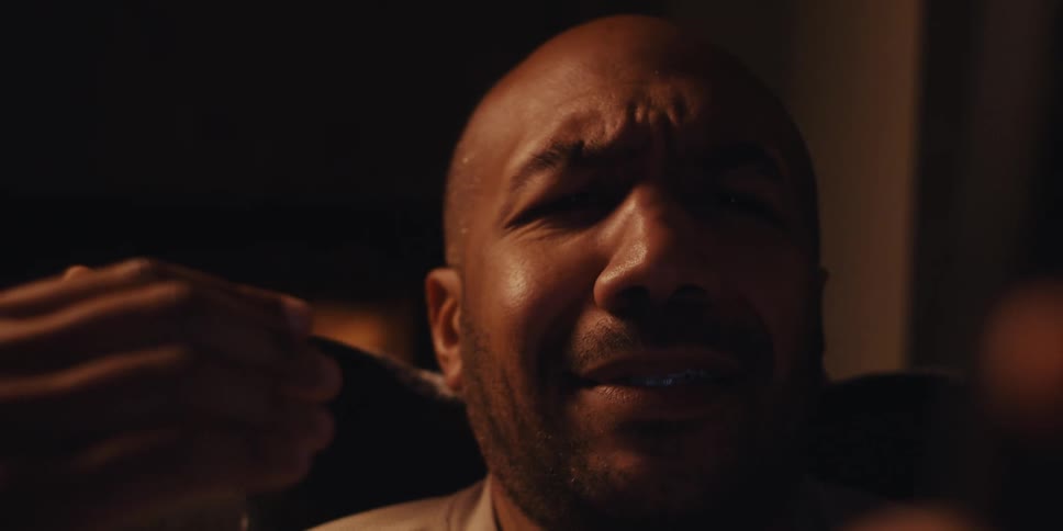 A man sits by the fire holding a smartphone and muttering in disbelief