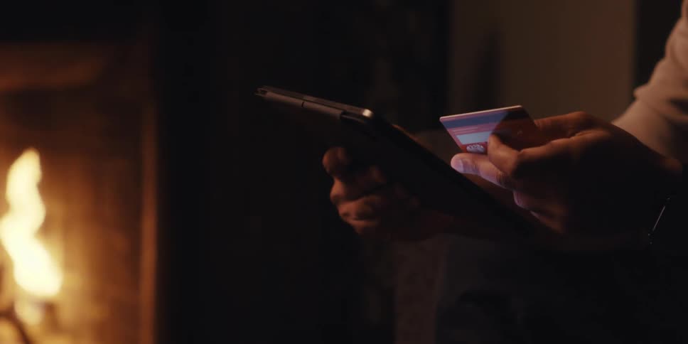 A man is holding his credit card and typing the number into the tablet