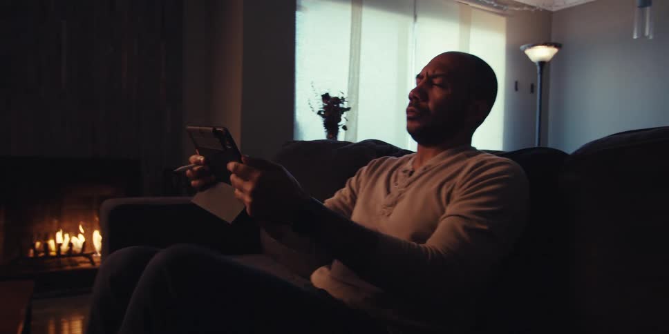 A man uses a pen on a tablet screen and then sits back on the sofa