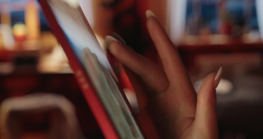 A womans hand with long manicured nails scrolling on a tablet screen