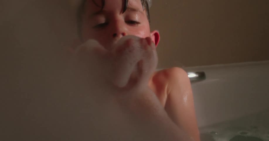 A boy blows bubbles in the bubble bath