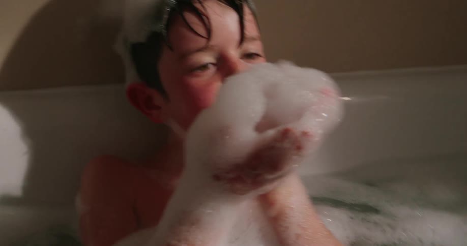 Young boy blowing suds off his hands while taking a bath