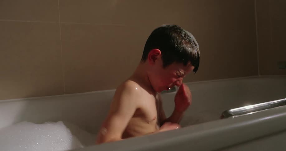 A child wipes his face in the bathtub