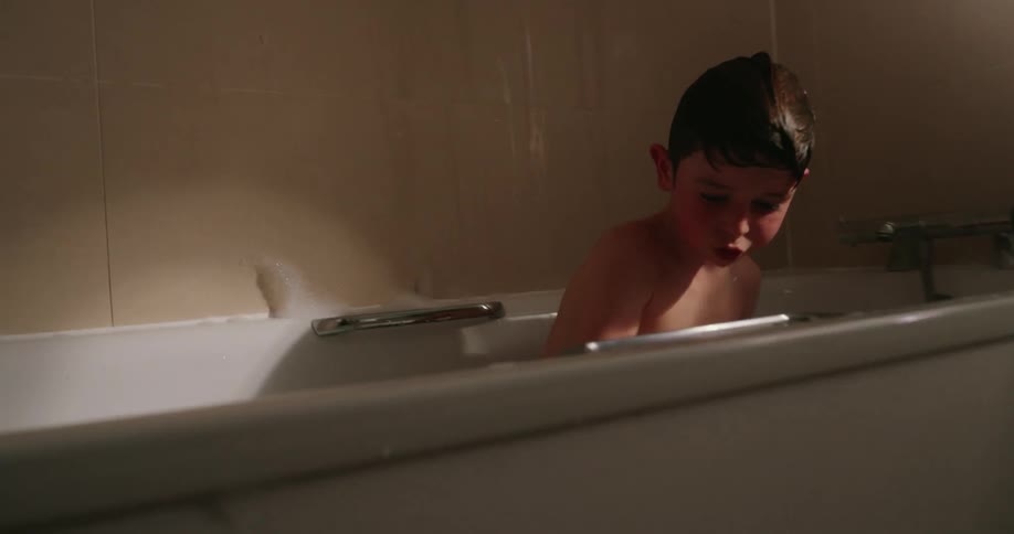 The little boy is playing with his toy in the bath tub that is full of water and bubbles