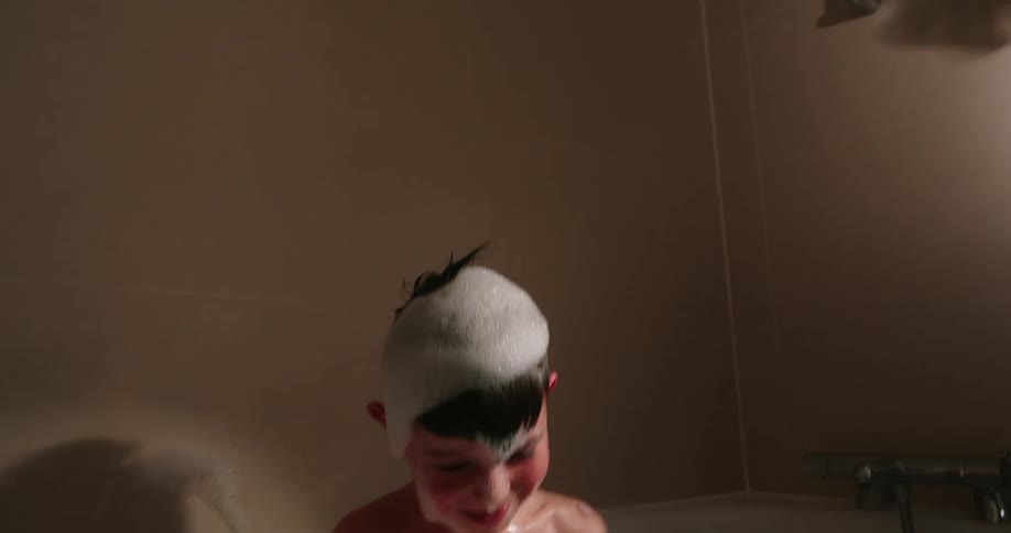 A boy takes a bath in a bathtub filled with soap bubbles arms raised playfully amidst the foam