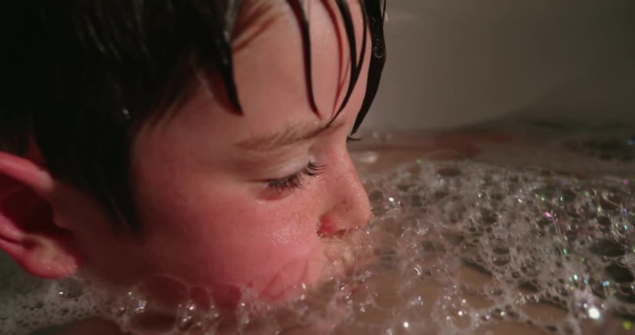 A young child is submerged in a bubble bath their face close to the bubbles as they enjoy the water