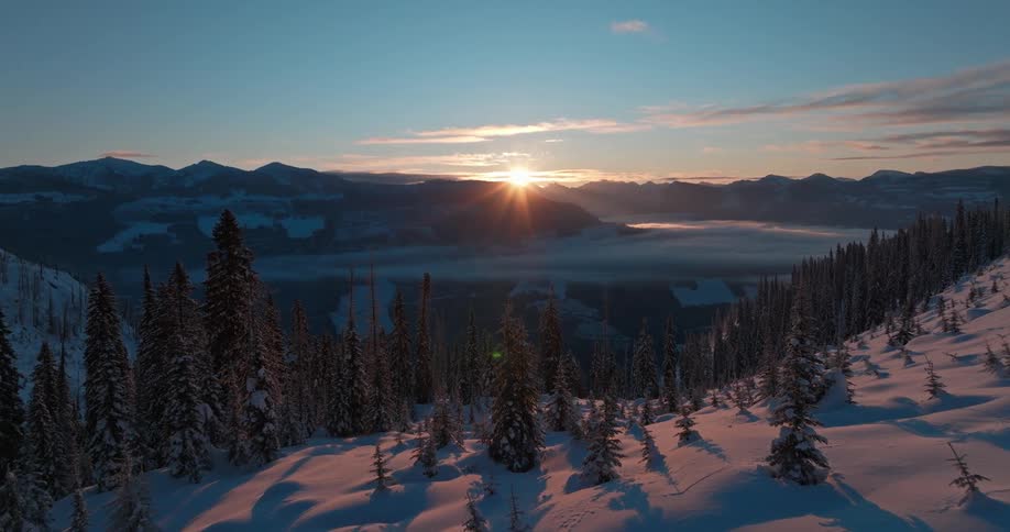 Aerial landscape of conifers in snowy mountains and sunrise on horizon