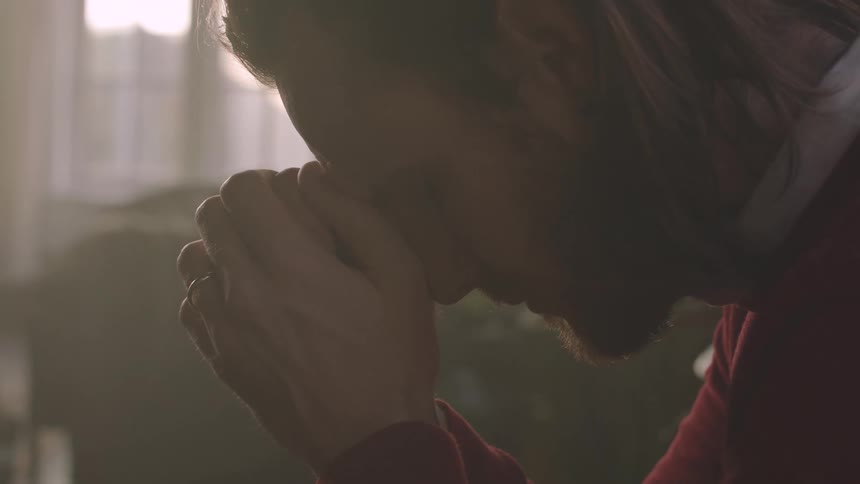 A person clasps their hands together possibly in a gesture of prayer or contemplation set against a softly lit background