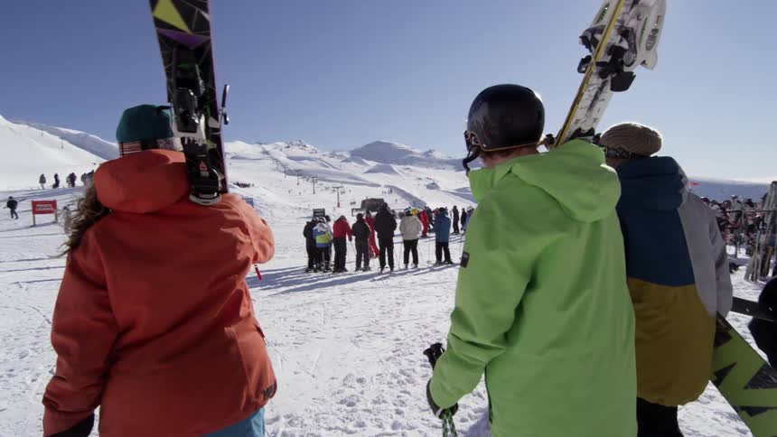 Skiers and a snowboarder walking towards a lift at a ski resort