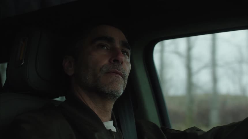 Older man smiles while driving past leafless trees during the daytime
