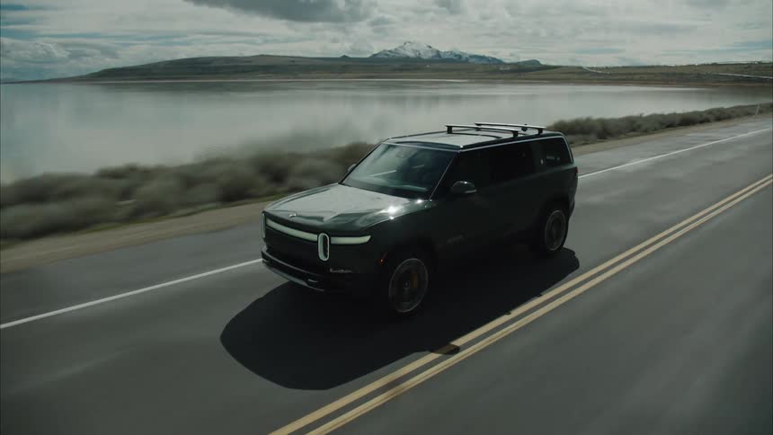 Sports utility vehicle drives along a highway past a lake on a cloudy day
