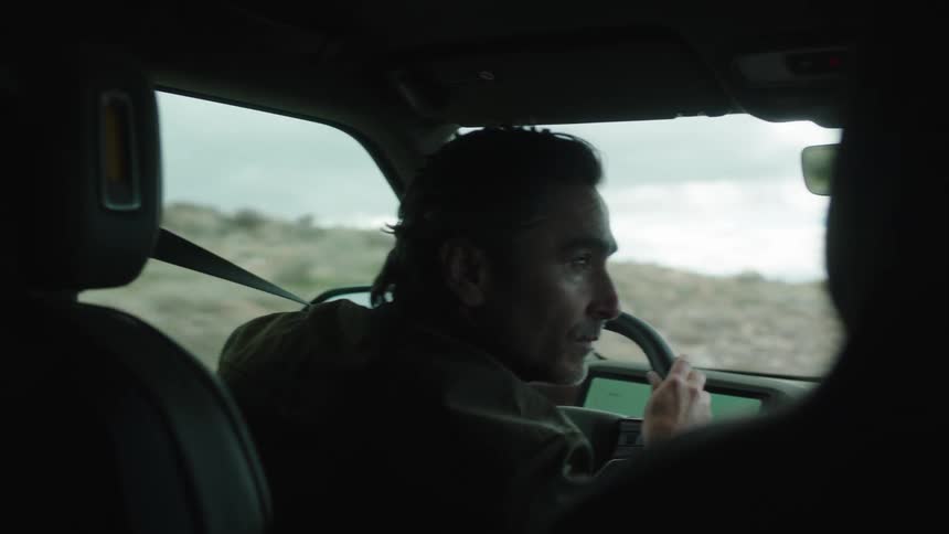 A person is driving a car with both hands on the steering wheel as the dashboard displays two screens with greenlit interfaces