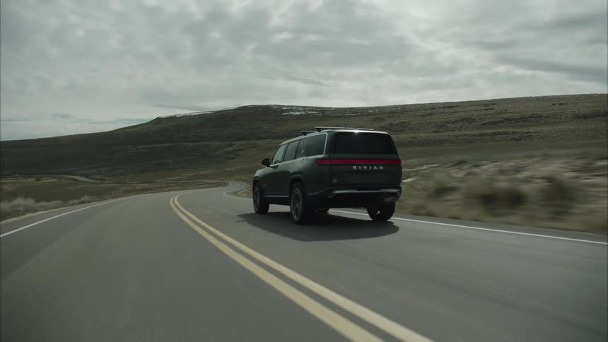 A rivian sport utility vehicle travels along a remote highway