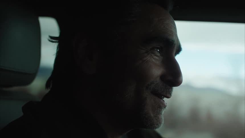A close up of the face of a man driving a car while talking