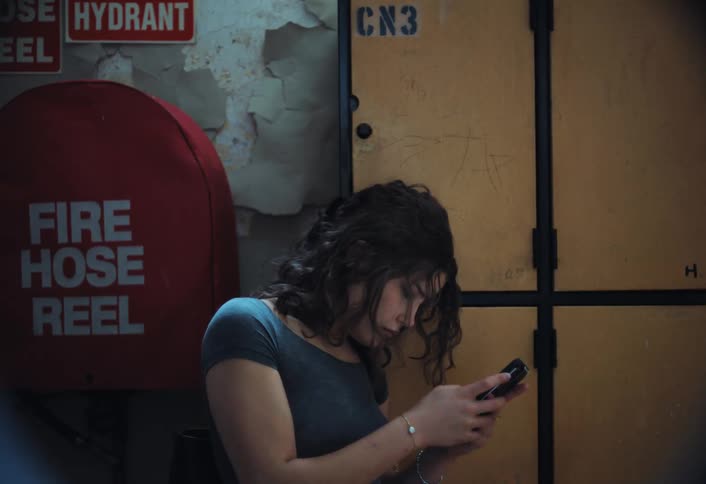 A young woman leaning against a yellow wall and texting in her phone