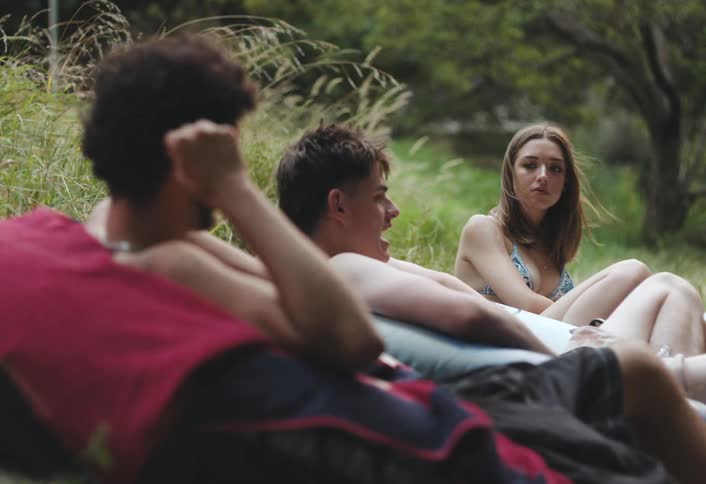 A group of friends in swimsuits relaxes on grass after swimming in a river