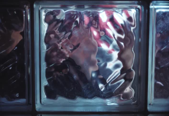 A distorted view of hands tapping against a textured glass block creating a warped visual effect