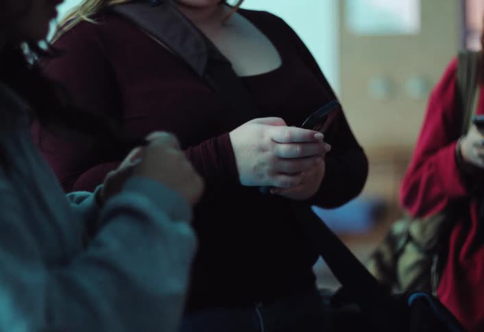 Woman texts on her smartphone while standing indoors near two other women during the day