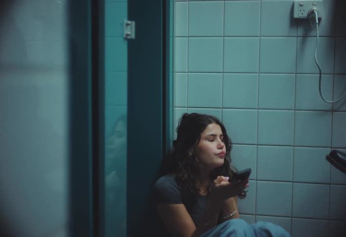 Girl smoking an electronic cigarette squatting on the floor while looking at her cell phone and talking to someone
