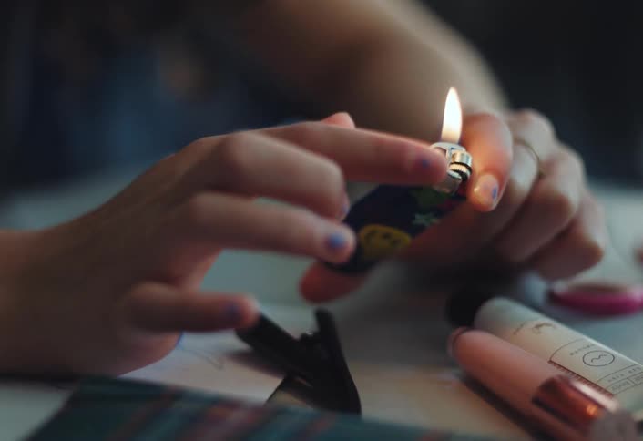 The female is holding a lighter lit and is moving her finger back and forth through the flame