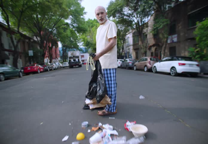 Man in pajamas holding a bag of garbage sees that it opened and everything ended up in the street