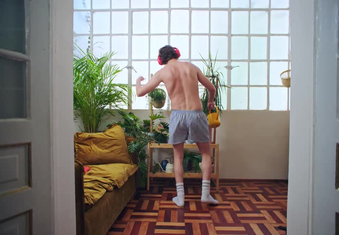 Man wearing headphones dancing in his underwear while watering plants indoors