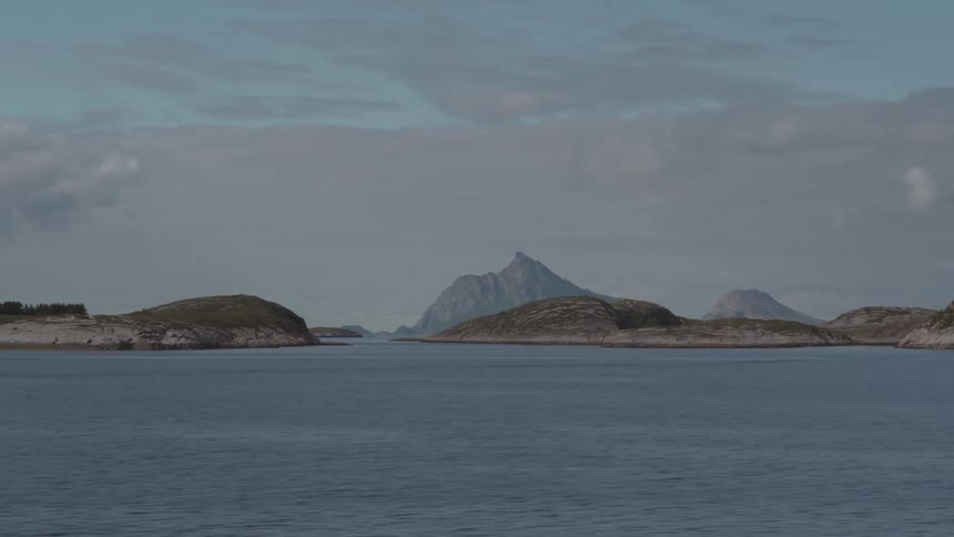 A serene seascape features several small rocky islands scattered across a calm blue body of water under a cloudy sky