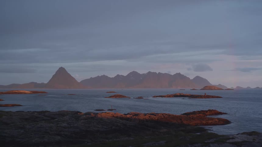 A scenic landscape shows dark rocky islands scattered across a body of water with silhouetted mountains in the distance under a dusky sky
