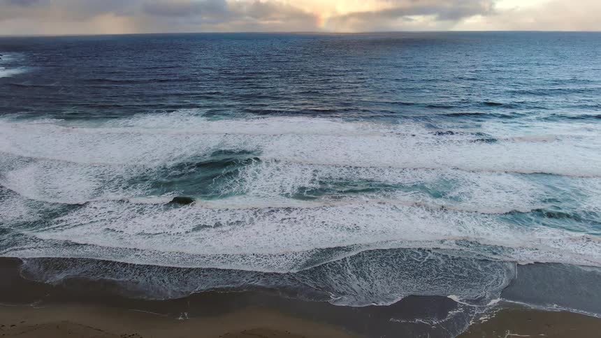 Aerial of the tide rolling onto sandy shoreline at sunrise