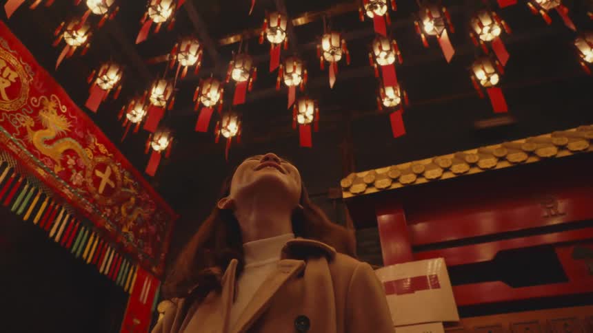 Woman wearing a coat smiles while looking around a building decorated in an east asian style