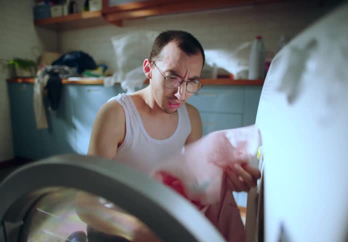 A man using a washing machine realizes a pink sock has stained all his clothes pink causing him to panic