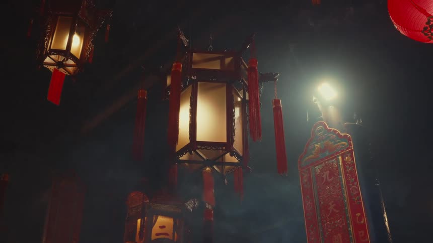 Lit lanterns hang against a dark background one illuminated by a bright light source