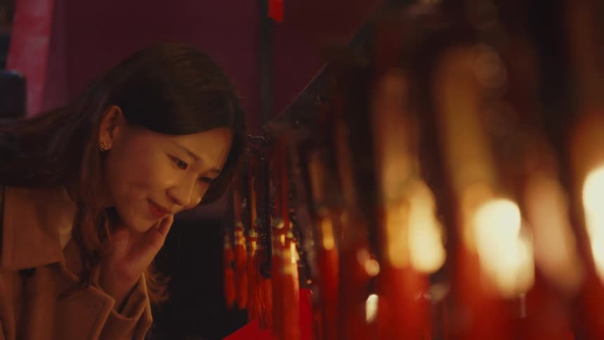 A woman observes a row of hanging red and gold ornaments under dim light