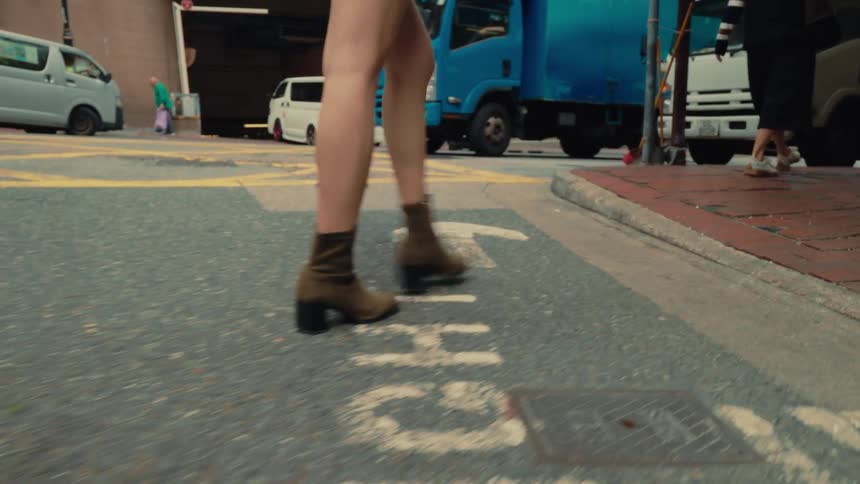 A woman wearing boots walks along a bustling city street