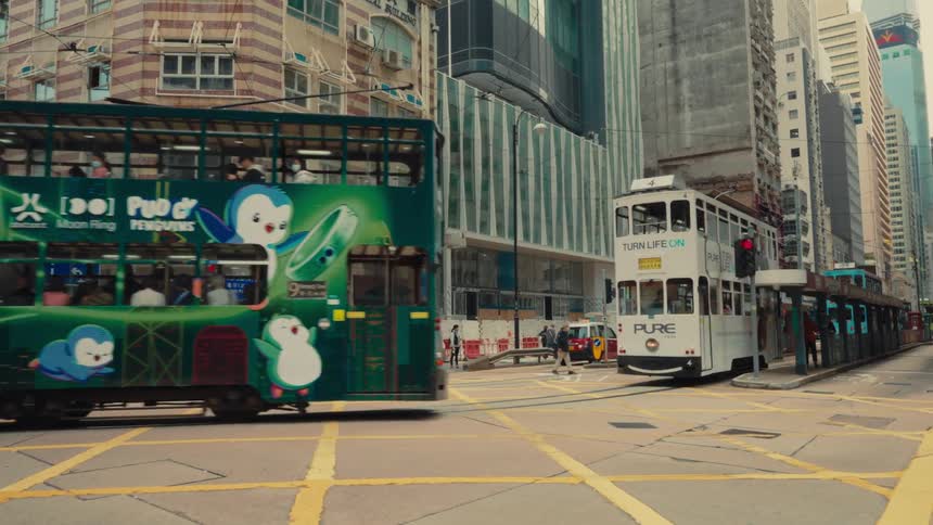 A green hong kong tram travels along a bustling city street amidst towering skyscrapers and yellow crosswalks