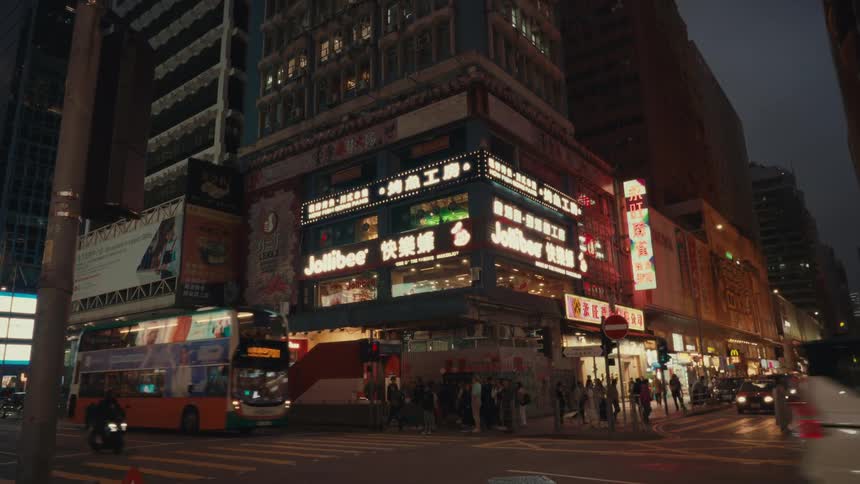 A busy hong kong street scene at night shows a doubledecker bus and other traffic with illuminated buildings including a prominent jollibee restaurant