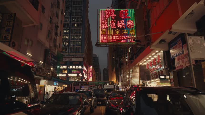 A bustling street scene in hong kong at night featuring a brightly lit neon sign with chinese characters overhead wires and a mix of vehicles and pedestrians