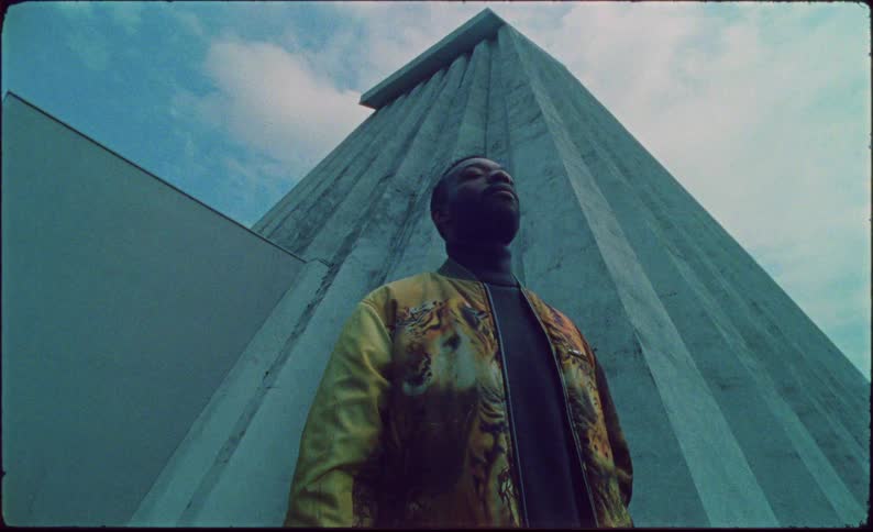 Man raises his head while standing near a tall building in a tiger patterned jacket
