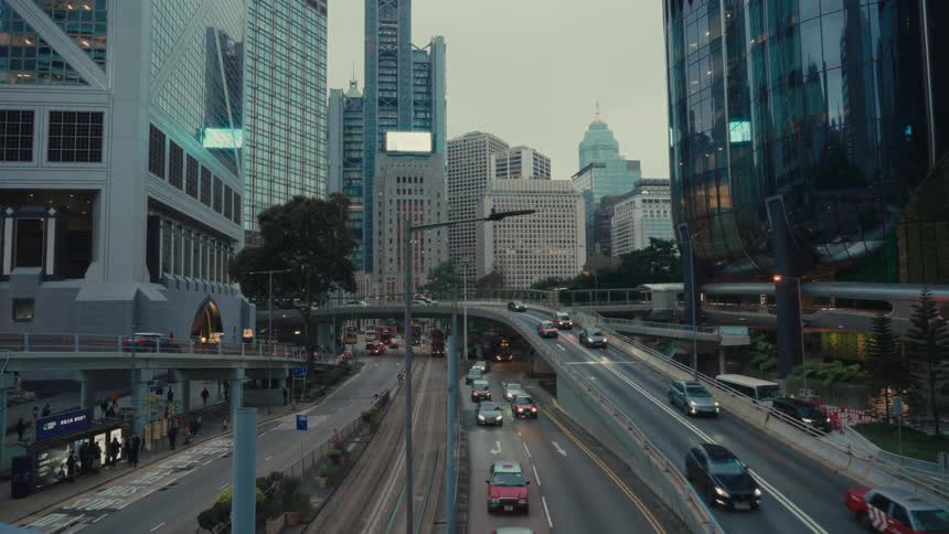 From a high vantage point a bustling hong kong highway showcases a flow of vehicles including iconic red taxis weaving through a dense landscape of towering skyscrapers under a soft overcast sky