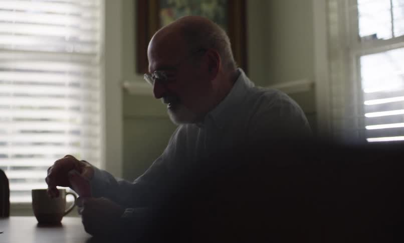 Elderly man sitting at the dining table smiles and gestures while playing cards