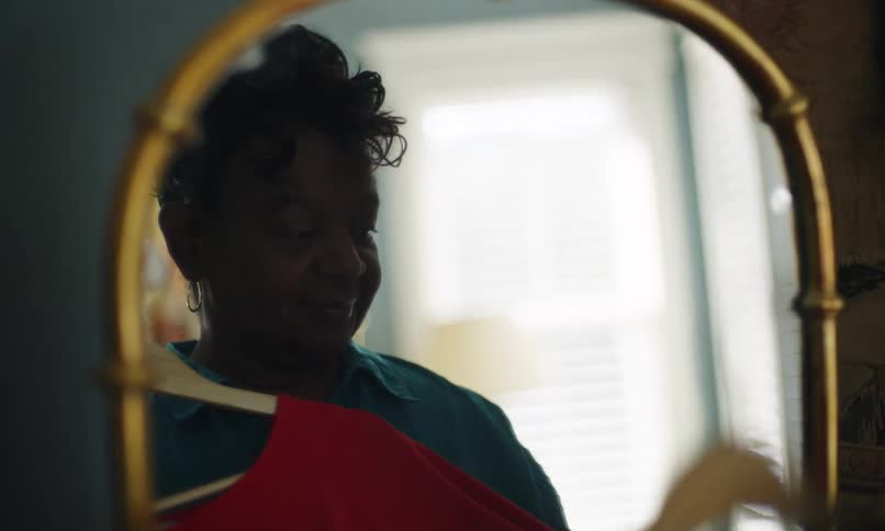 A woman holds up a shirt on a hanger in front of herself in the miirror