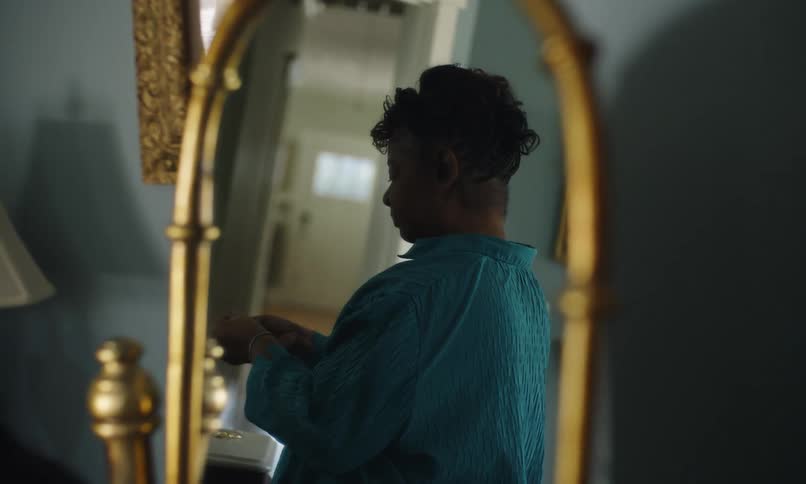 A woman tries on earrings in front of a goldrimmed mirror in a dimly lit room