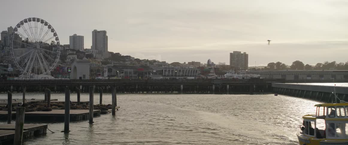 A yellow boat moves with purpose away and across the waters of san francisco bay set against the backdrop which features the iconic cityscape and waterfront eventually departing from the view entirely