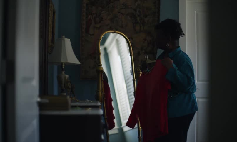 Lady approaches a mirror with a dress in her hand